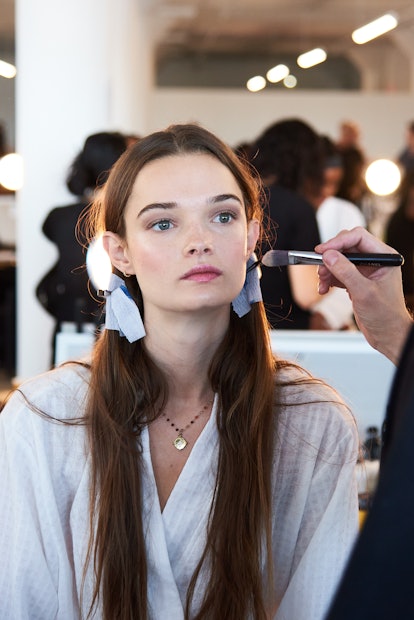 Woman with brown hair and pigtails getting her makeup done. 